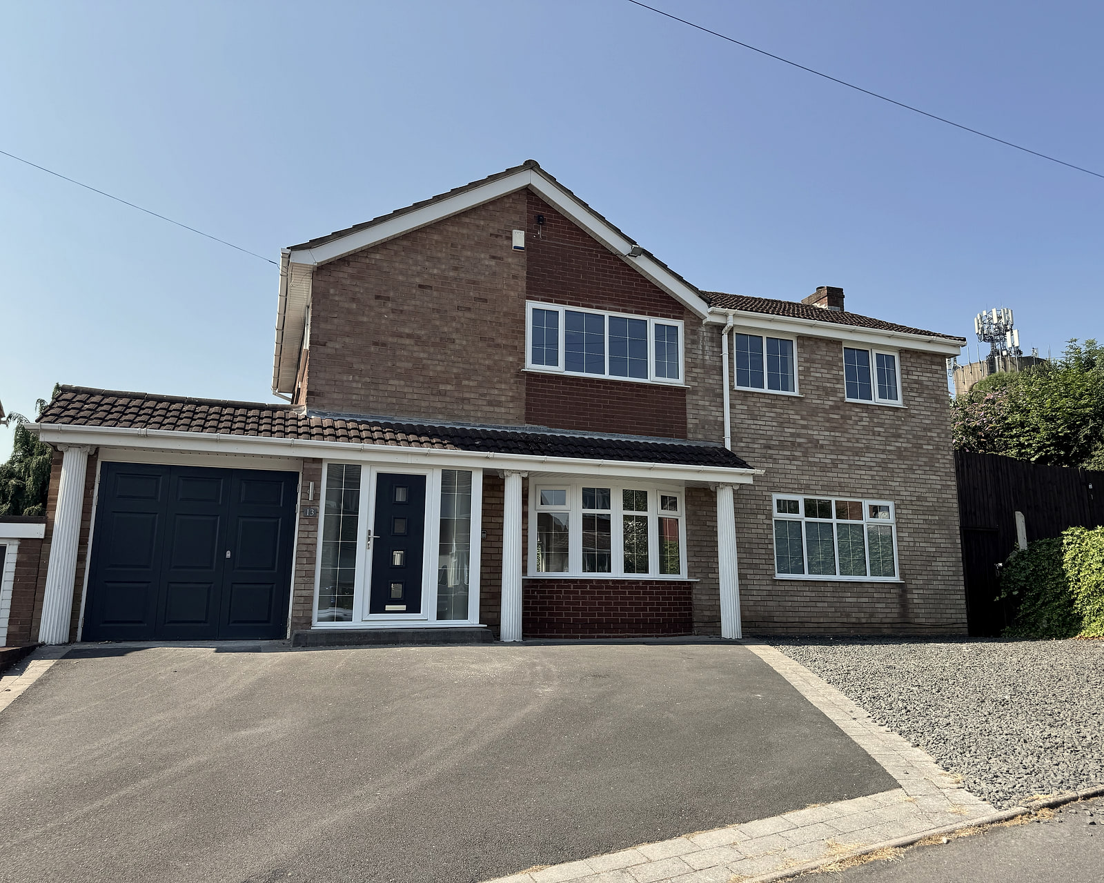 A detached brick house with a dark front door and garage, driveway to the front, on a sunny day.