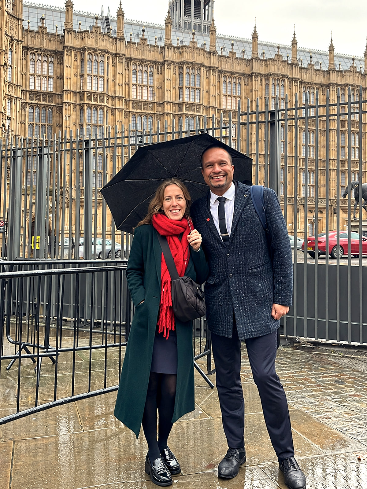 Louis Stedman-Bryce and Carly sharing an umbrella outside the Palace of Westminster on a wet day.